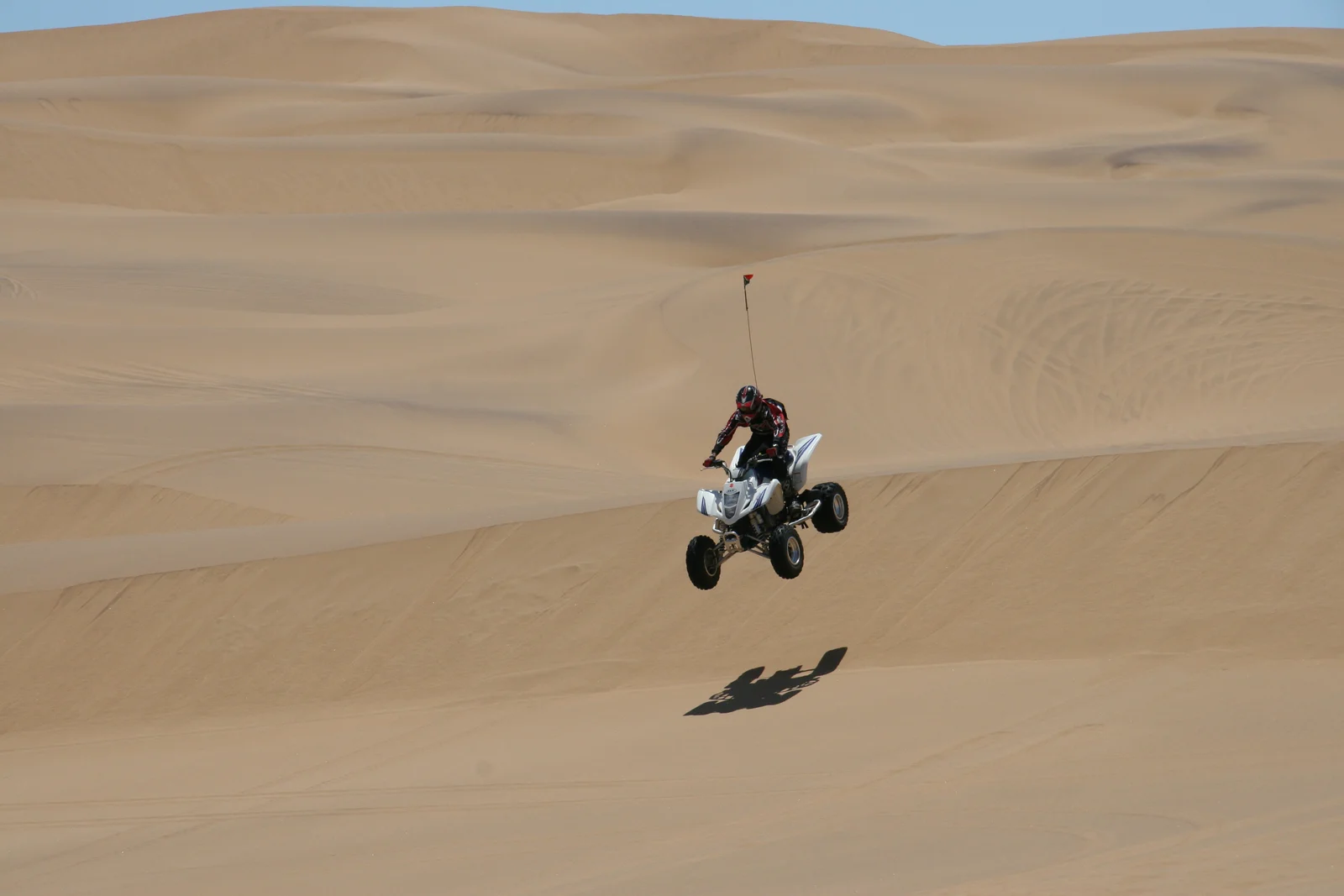 A helmeted rider jumps a white sport ATV over sand dunes.