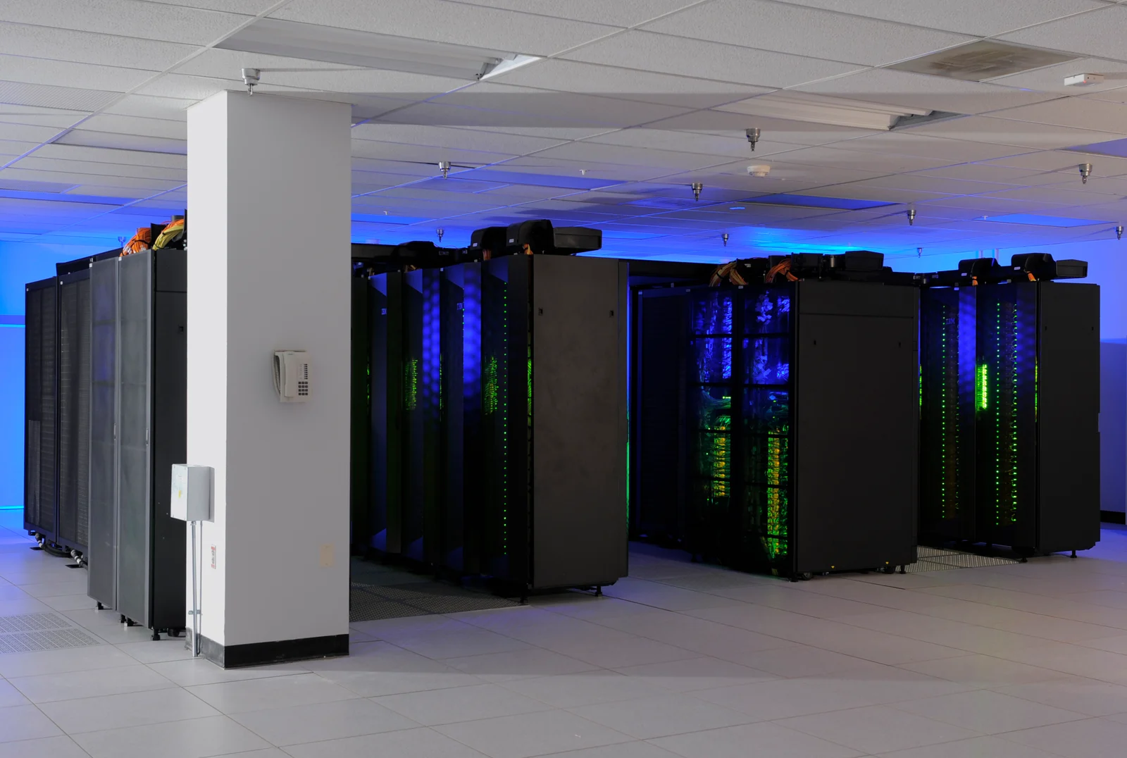 Rows of black computer cabinets inside NASA’s Discover supercomputer facility, illuminated by blue and green light.