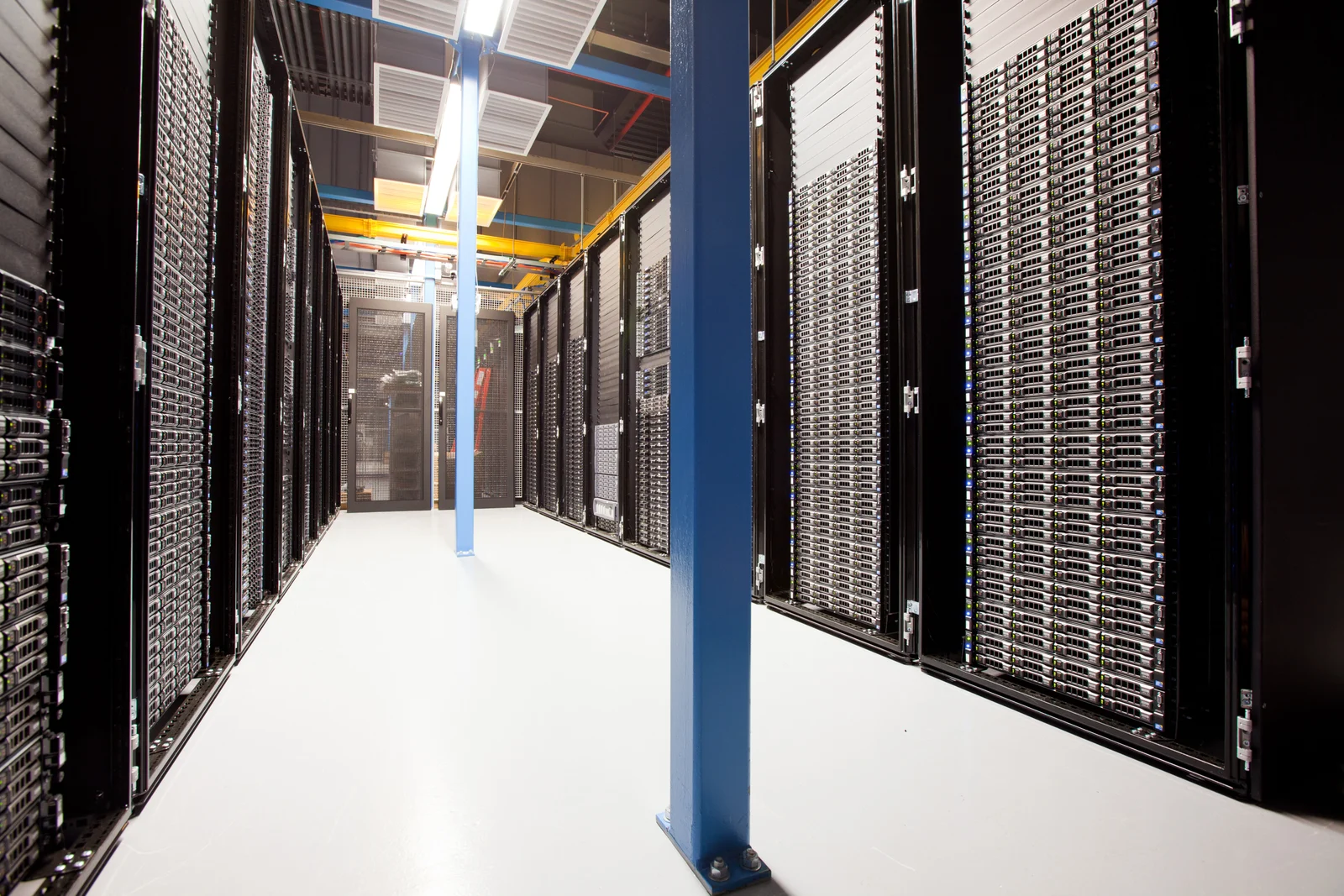 A brightly lit aisle between rows of black server racks filled with silver rack-mounted computers.