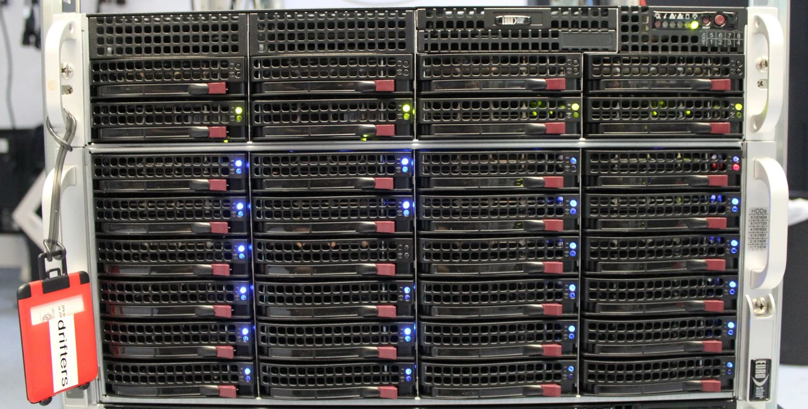 Front of a storage server containing rows of removable drive bays with illuminated status indicators.