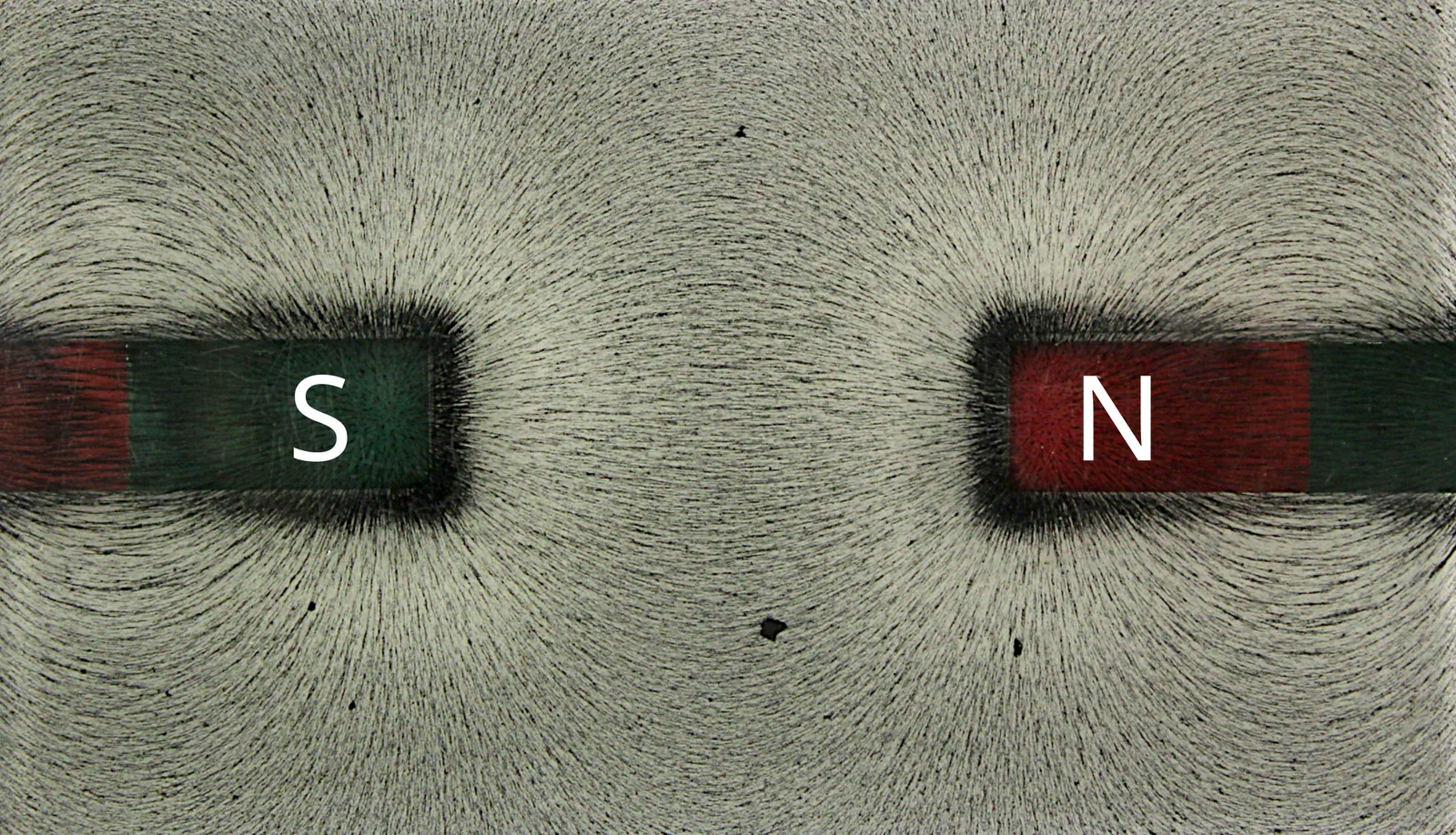 Iron filings arranged along the magnetic field lines of two attracting bar magnets, illustrating interacting forces between elements